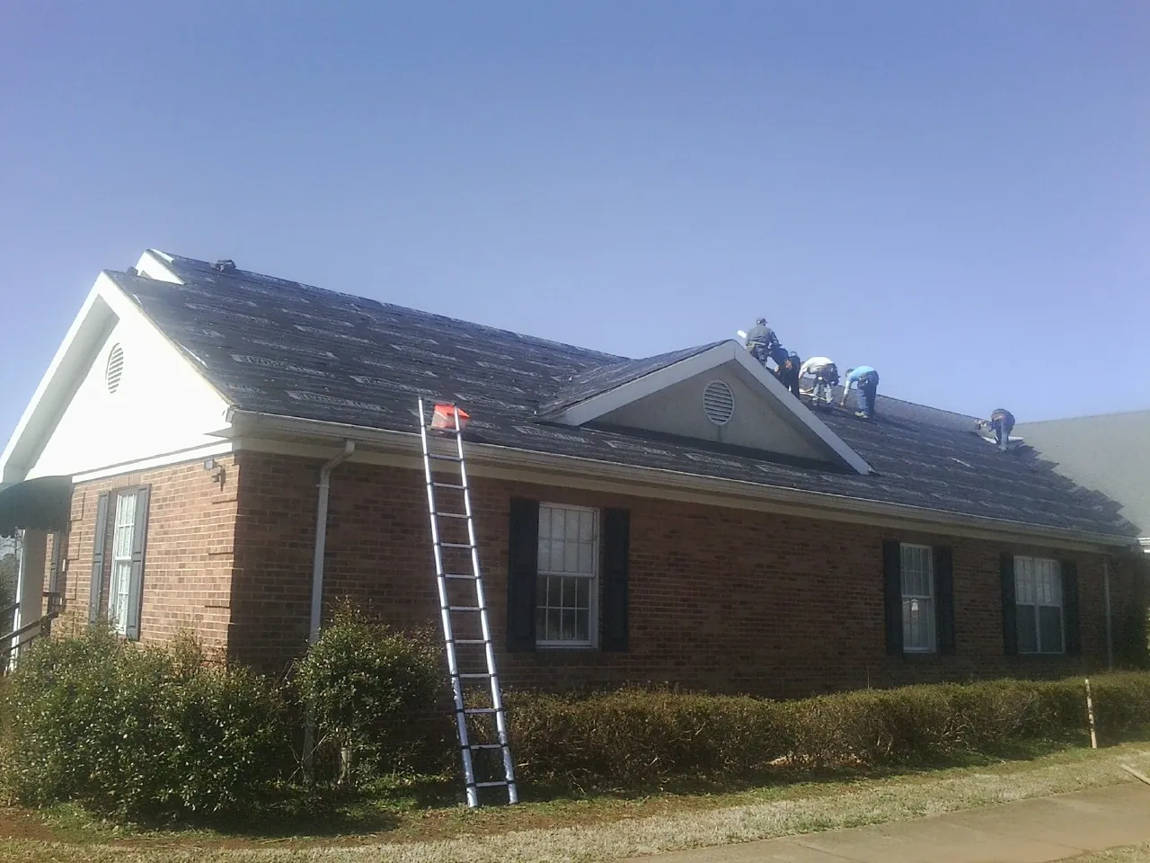 Crew tearing shingles off a brick ranch roof with a ladder set — Metal Roof Repair work by our crew in Inglewood