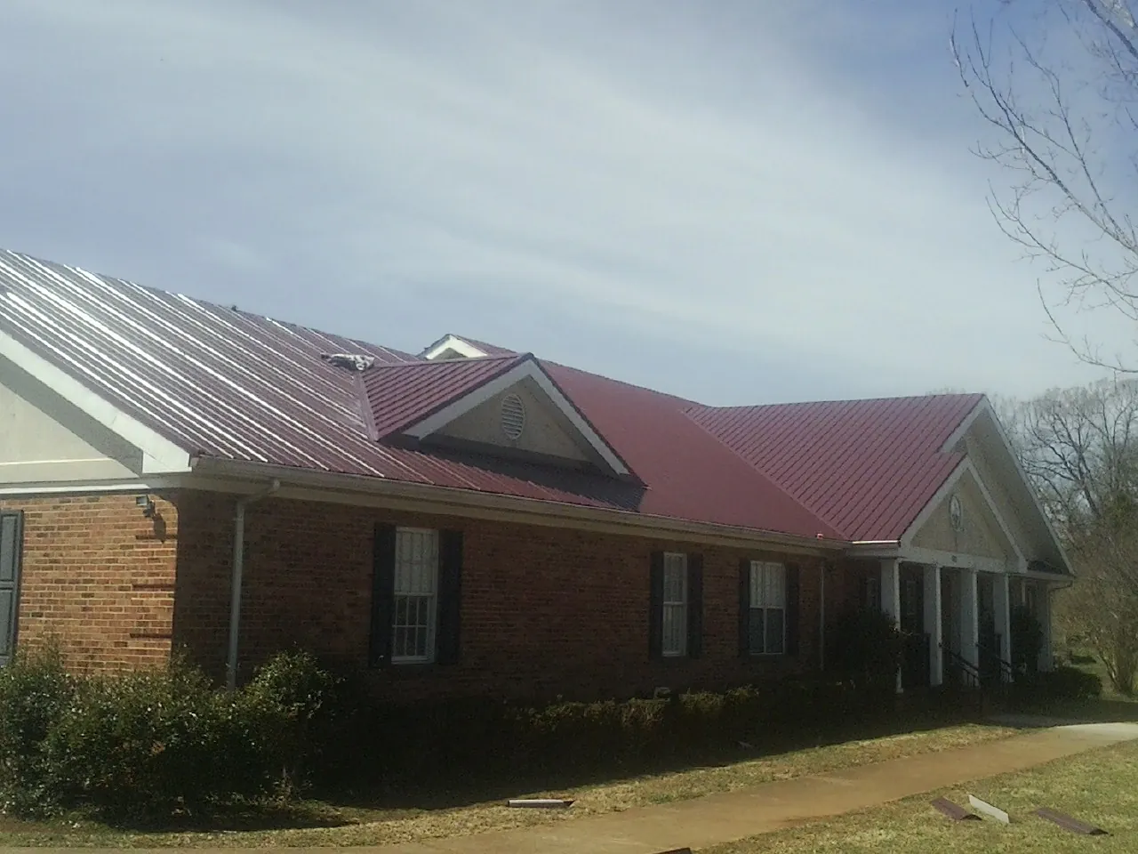 Red metal roof with gabled entries on a long brick building, from a Hail Damage Roof Repair job in Inglewood