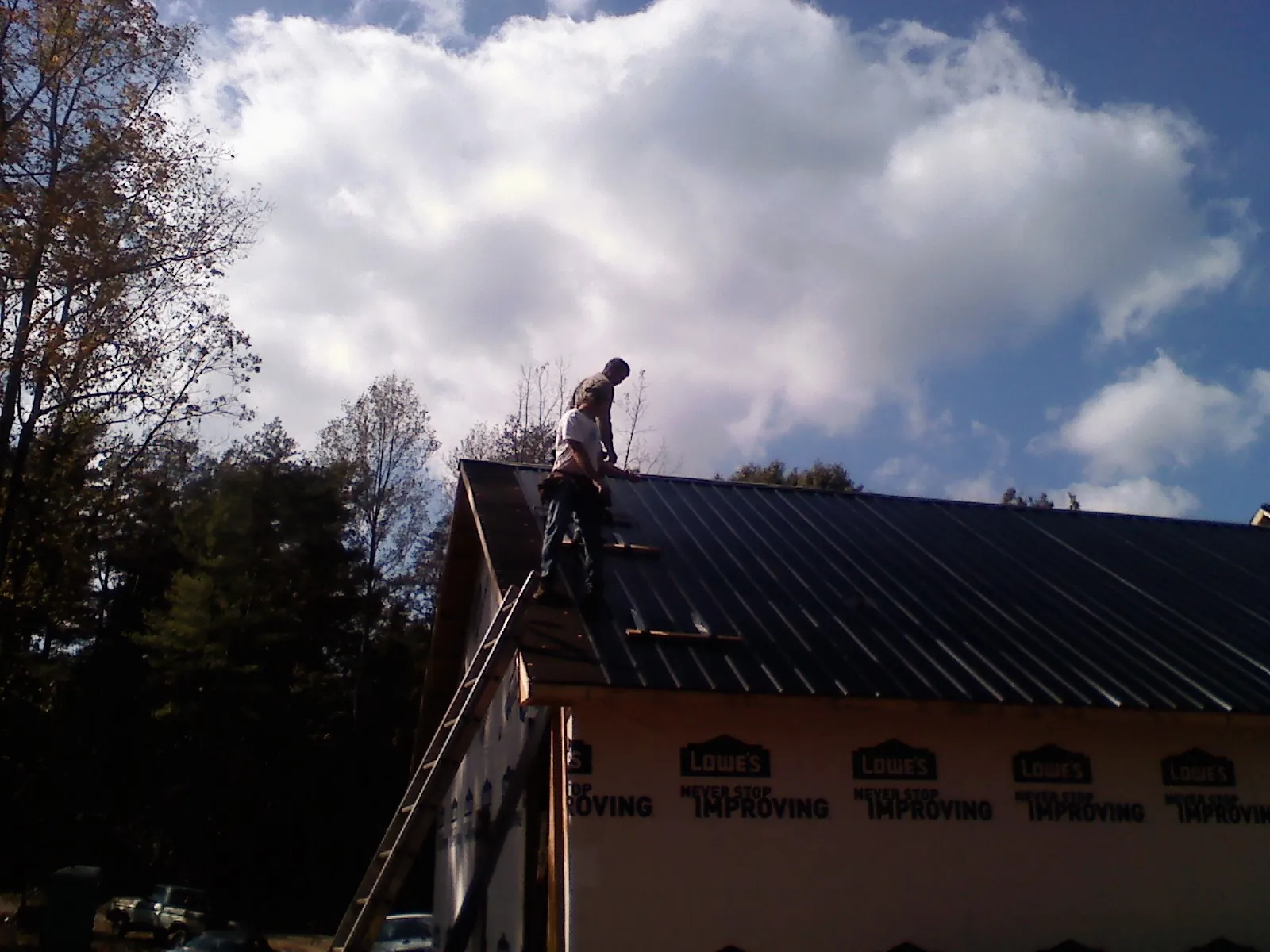 Roofer fastening dark metal panels high against a cloudy sky, from a Roof Inspection job in Inglewood