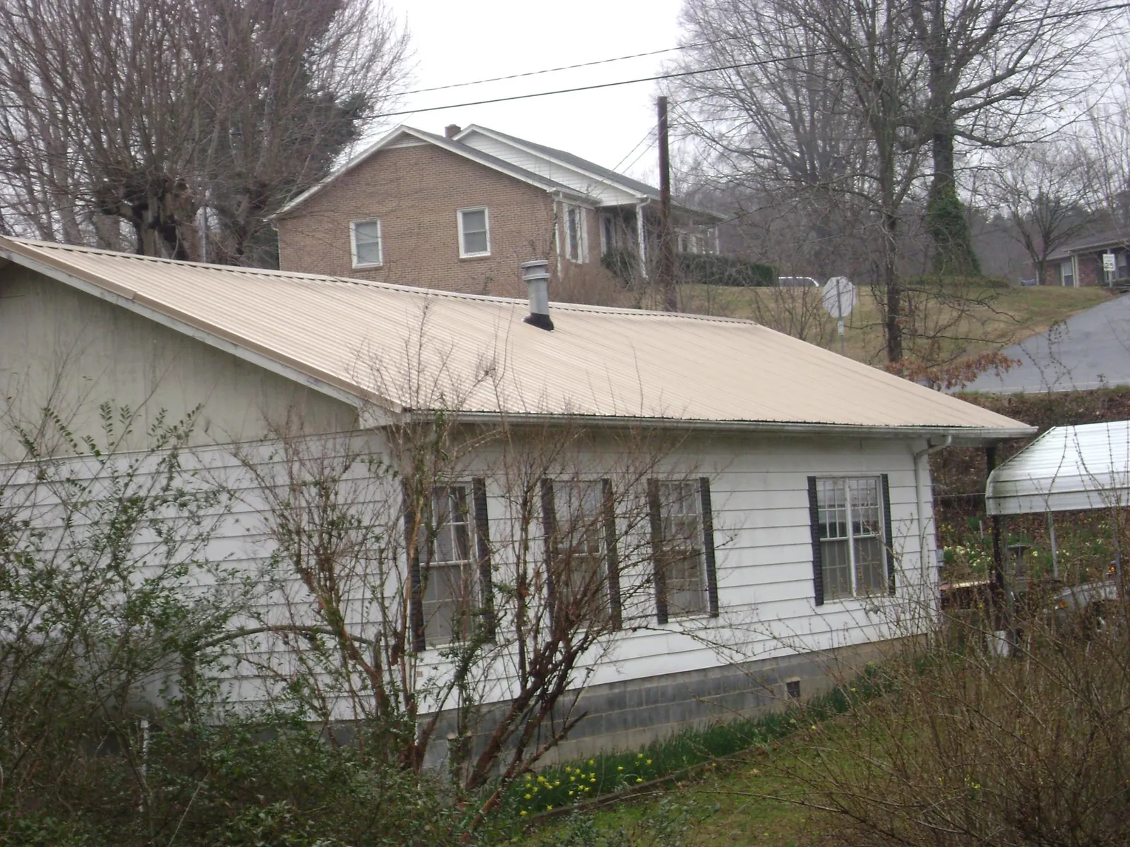 Tan metal roof on a white sided house set into a hillside — Commercial Roofing by Roofing Brothers in Inglewood